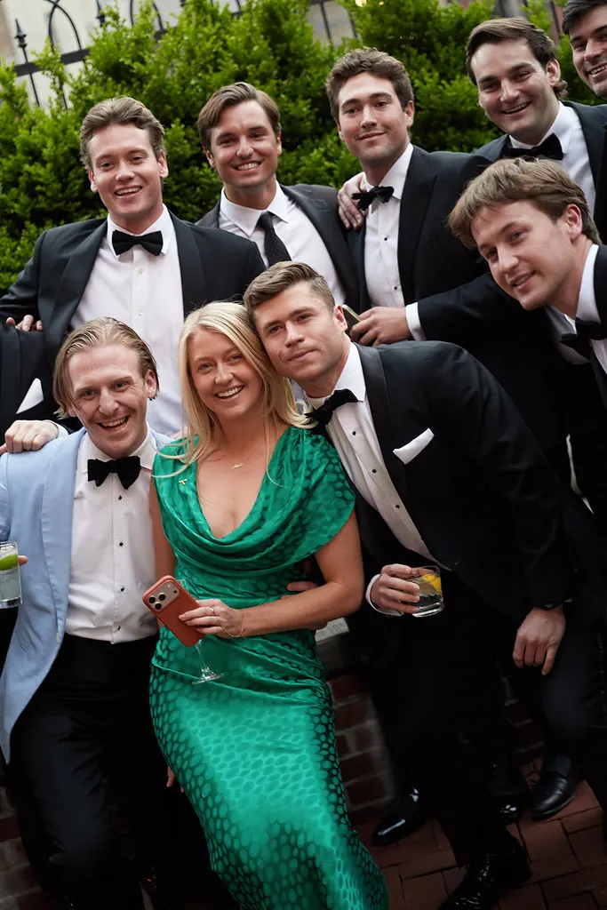 A guest in an emerald dress surrounded by friends in black tie.